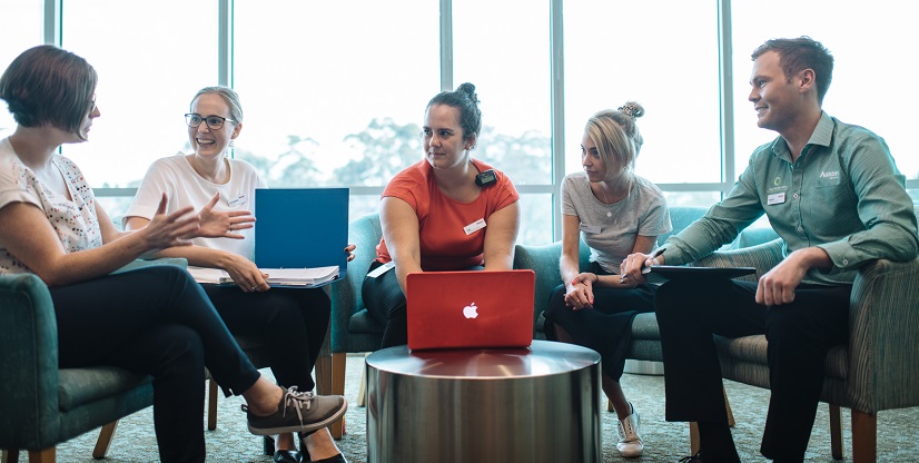 A group of allied health professionals with laptops and folders are having a discussion